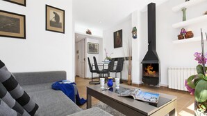 Ein Wohnzimmer mit Sofa, Couchtisch und Kamin. An der Wand hängen Bilder und ein Durchgang zu einem anderen Raum.