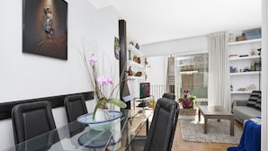 Ein modernes Wohnzimmer mit einem Glastisch, schwarzen Stühlen, einem grauen Sofa und einem Bücherregal voller Dekoration.