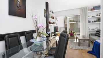 Una sala de estar moderna con una mesa de comedor de vidrio, sillas negras, un sofá gris y una estantería llena de objetos decorativos.