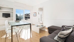 A modern living room with a glass dining table, white chairs, a grey sofa, and a coffee table.