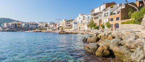 A coastal town with colorful buildings along the waterfront, clear blue water, and rocky shore.