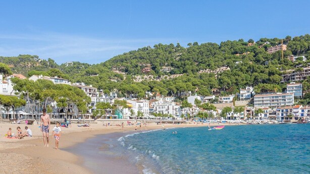 A coastal town with a beach, clear blue water, and buildings on a hillside.