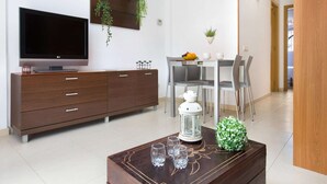 Una sala de estar moderna con un televisor de pantalla plana, un mueble de madera, una mesa de comedor con sillas y una mesa de centro con vasos y un objeto decorativo.