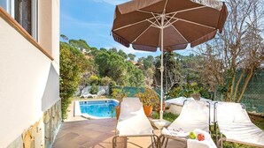 Un patio con piscina, sillas de descanso y una sombrilla.