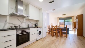 Una cocina moderna con horno integrado, microondas y lavadora, un comedor con sillas de madera y un ventanal que proporciona luz natural.