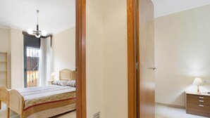 Un dormitorio con cama, mesita de noche, silla, armario y ventana con cortinas.