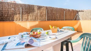 Una terraza con una mesa dispuesta para el desayuno, que incluye frutas, un periódico y una taza.