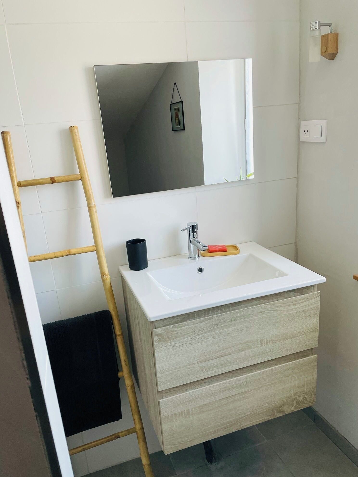 Ein Badezimmer mit weißem Waschbecken, einem Spiegel, einer Holzleiter und einem schwarzen Handtuch.