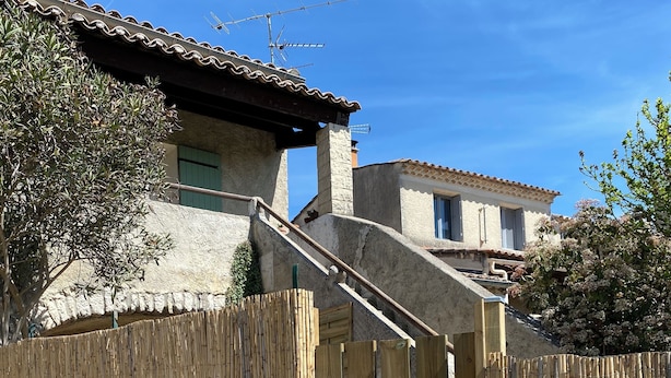 A rustic house with a wooden gate, a stone wall, and a clear blue sky.