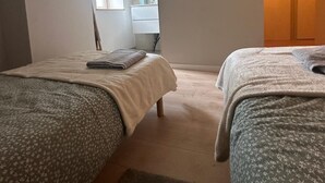 A bedroom with two beds, a window, a bathroom with a mirror, and a door leading to another room.