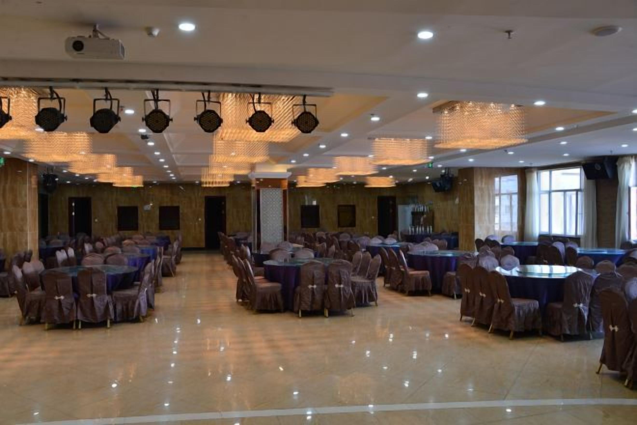 A banquet hall with tables arranged in rows, a stage with a podium, and a large window on the right.