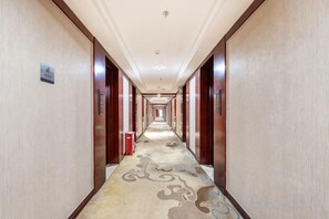 Un couloir d’hôtel avec un sol recouvert de moquette, des portes en bois et une poubelle rouge.