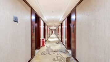 A long, narrow hotel corridor with a patterned carpet, wooden doors, and a red trash bin.
