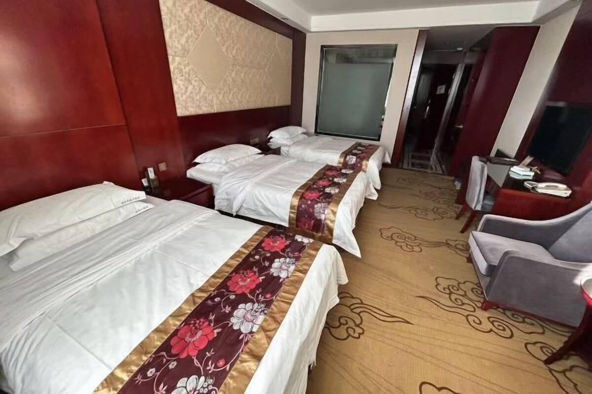 A hotel room with two beds, a desk, a chair, and a large window.