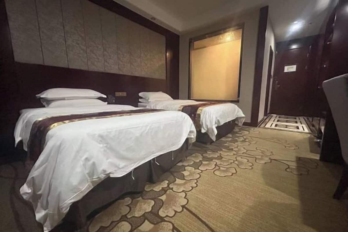 A hotel room with two beds, a large window, a carpeted floor, and a door.