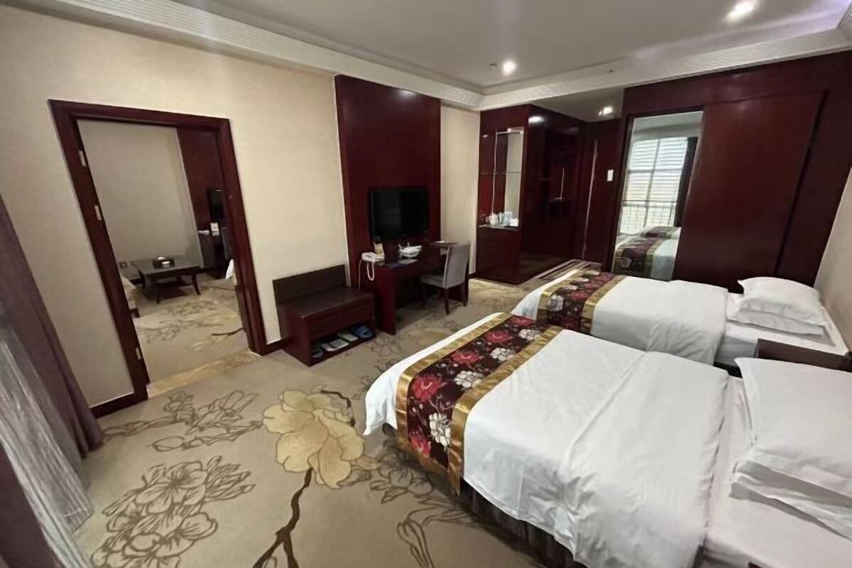 A hotel room with two beds, a TV, a desk, and a mirror.
