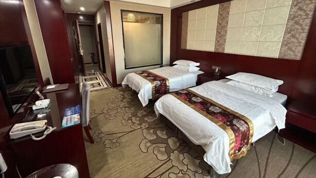 Une chambre d’hôtel avec deux lits, un bureau avec un téléphone, une chaise, une grande fenêtre et un sol recouvert de moquette.