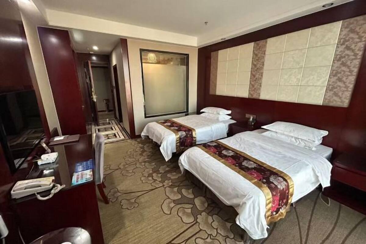 A hotel room with two beds, a desk with a telephone, a chair, a large window, and a carpeted floor.