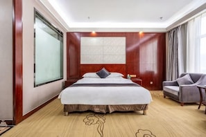 Quarto de hotel com cama grande, sofá, mesa de cabeceira e janela.