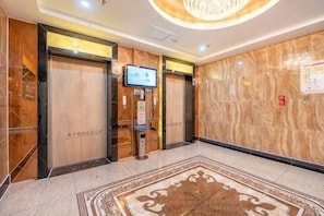 Um saguão de hotel com paredes de mármore, um quiosque digital de informações e um carpete estampado.