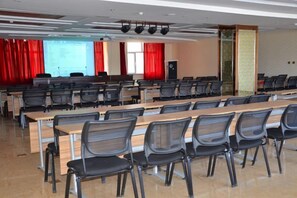 Une salle de conférence avec des rangées de tables et de chaises, un écran de projection et un pupitre pour les présentations.