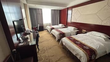 A hotel room with two beds, a desk with a computer, a TV, and a large window with curtains.