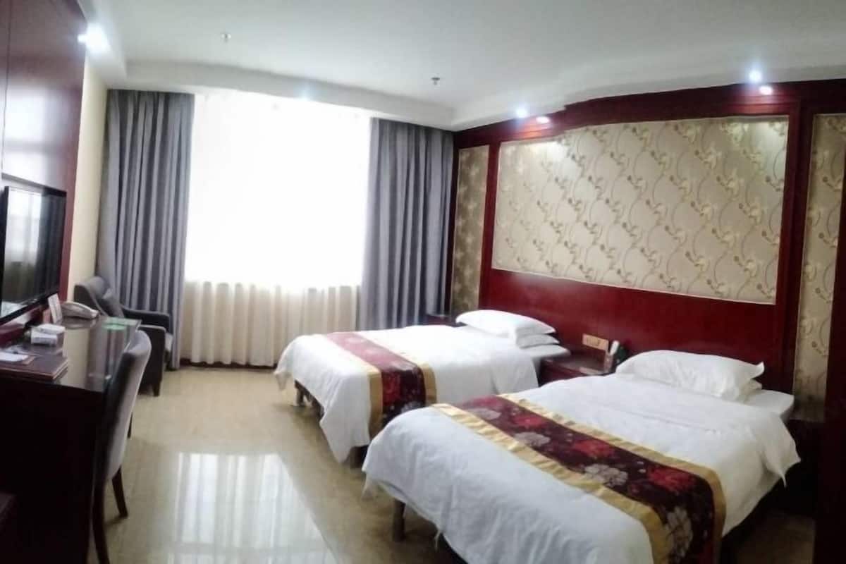 A hotel room with two beds, a desk, and a large window with curtains.