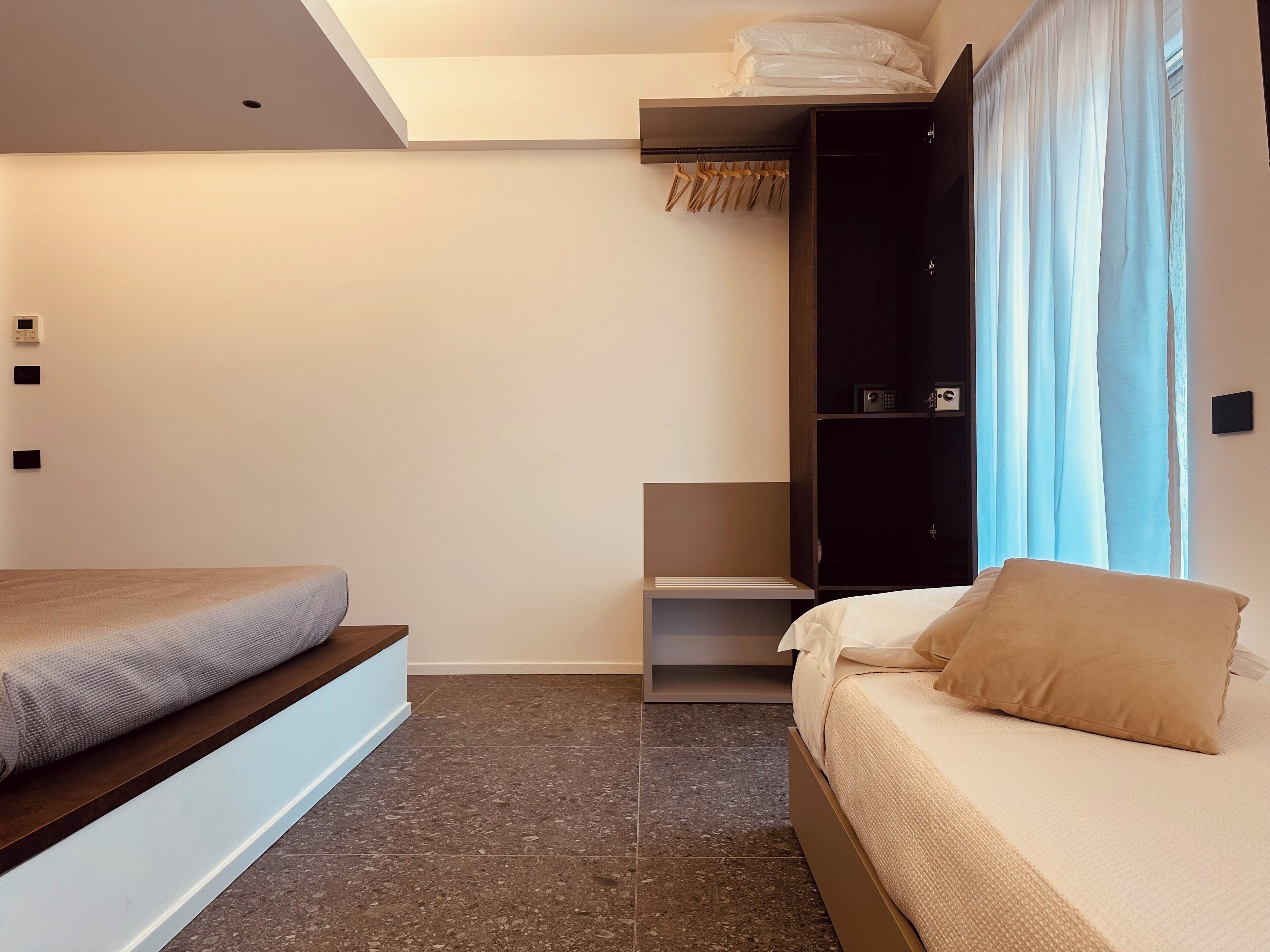 A modern bedroom with two beds, a wardrobe, and a small shelf unit.