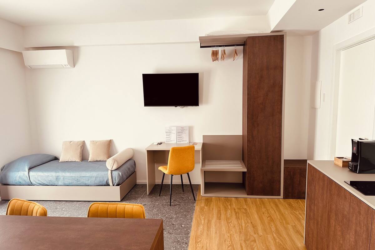 Ein kleines Hotelzimmer mit Bett, Schreibtisch, Stuhl und Fernseher.