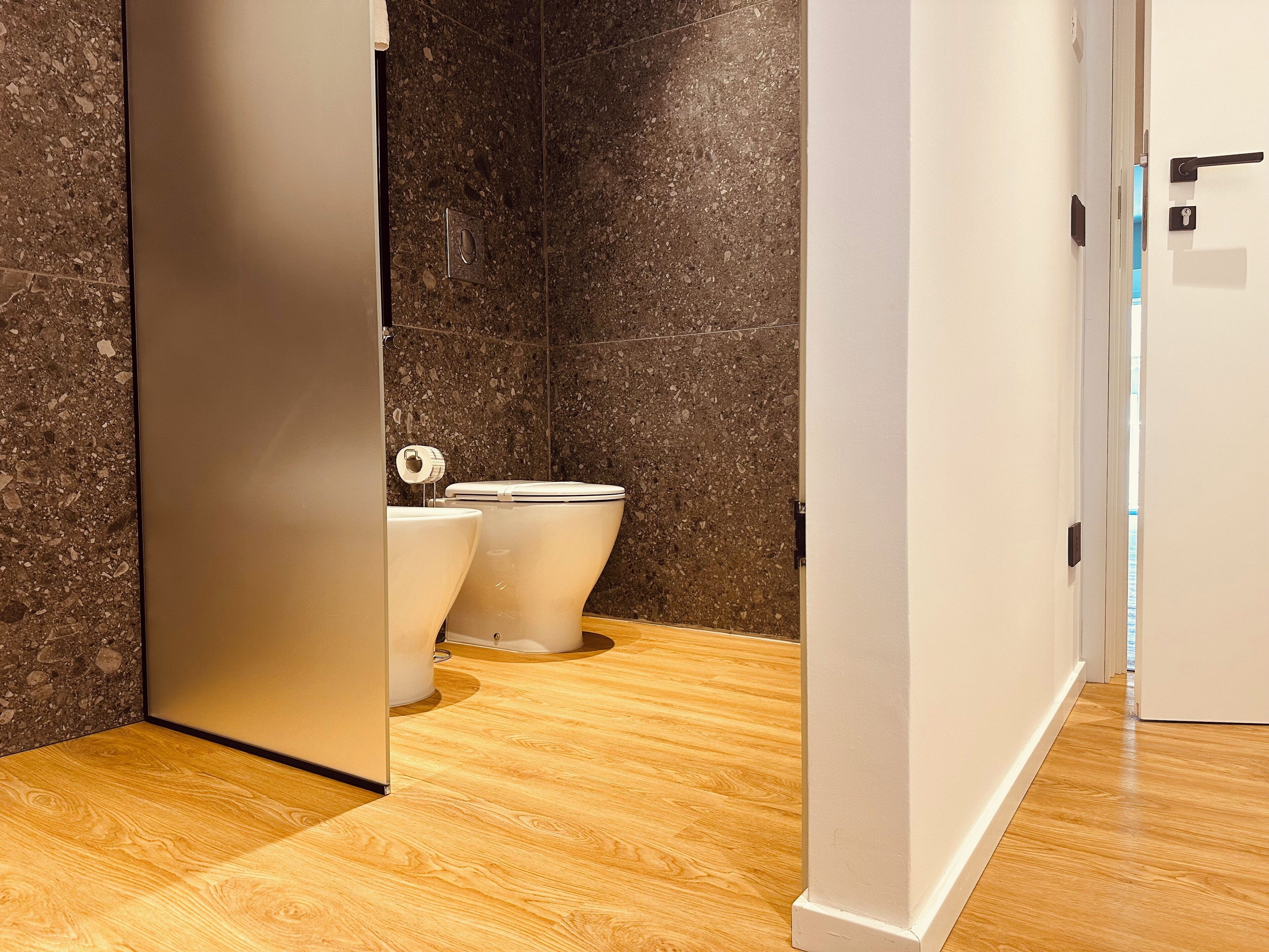 Een moderne badkamer met twee toiletten, een marmeren wand en een houten vloer.
