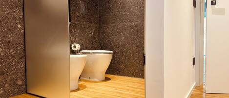 Une salle de bain moderne avec deux toilettes, un mur en marbre et un revêtement de sol en bois.