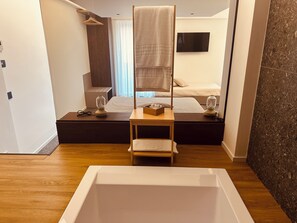 Un dormitorio moderno con una cama grande, lámparas de noche, una mesita de noche de madera y una bañera amplia.