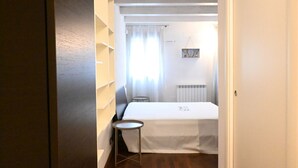 Una habitación con cama, una mesita, un radiador y una ventana con cortinas.