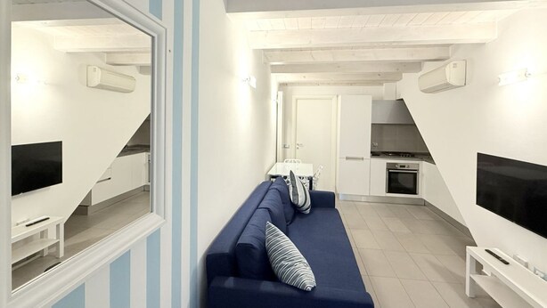 Una sala de estar moderna con un sofá azul, un televisor y un comedor con mesa y sillas.