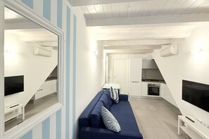 Un salon moderne avec un canapé bleu, un téléviseur et un coin repas comprenant une table et des chaises.