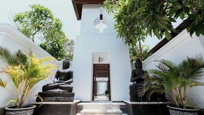 Egy nyugalmas udvar, melyben két nagy Buddha-szobor áll, mindkettő emelvényen, és amelyet virágtartókban elhelyezett növények, valamint egy fehér épület, melynek fa tetőszerkezete van, vesz körül.