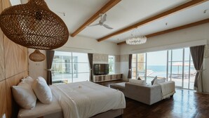 A spacious bedroom with a large bed, a sofa, a TV, and a balcony with a view of the sea. - Nalas Villa (Sukawati)