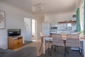 Un espace de vie compact comprenant un téléviseur, un canapé, une table à manger, des chaises, un coin cuisine et un ventilateur de plafond.