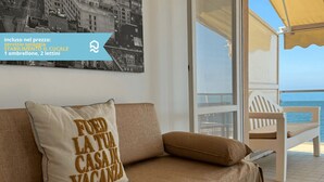 Un balcon avec vue sur la mer, une chaise blanche et un coussin orné d’un motif textuel.