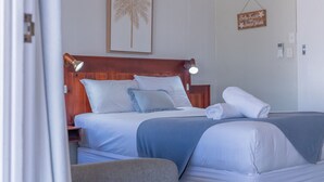 A hotel room with a wooden headboard, two beds with white and blue bedding, a framed palm tree artwork, and a sign on the wall. - Pacific Sun Bargara ~ by the beach (Bargara)