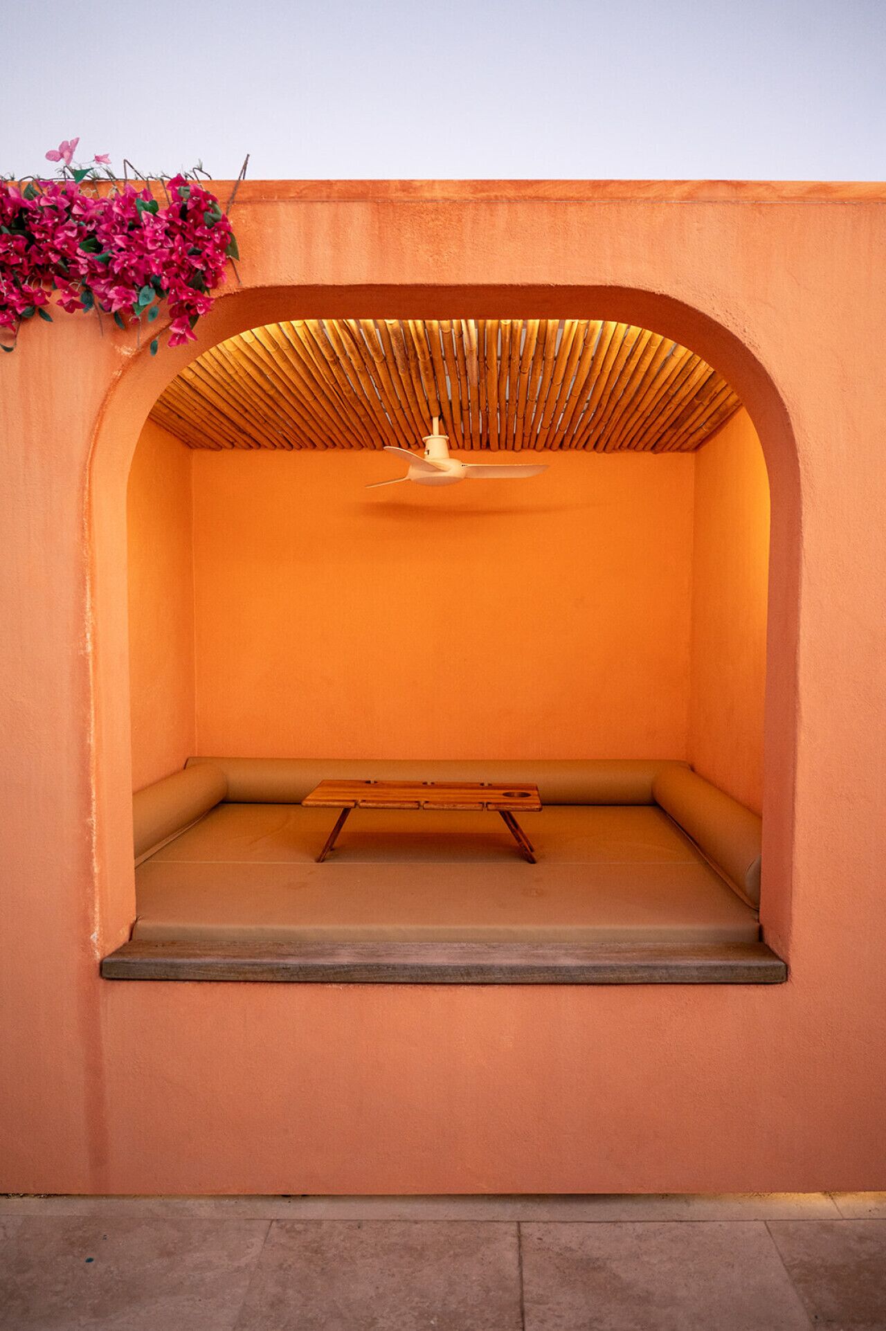 An arched seating area with a ceiling fan, a bench, and a wall with a bamboo ceiling.