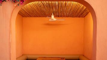 An arched seating area with a ceiling fan, a bench, and a wall with a bamboo ceiling.