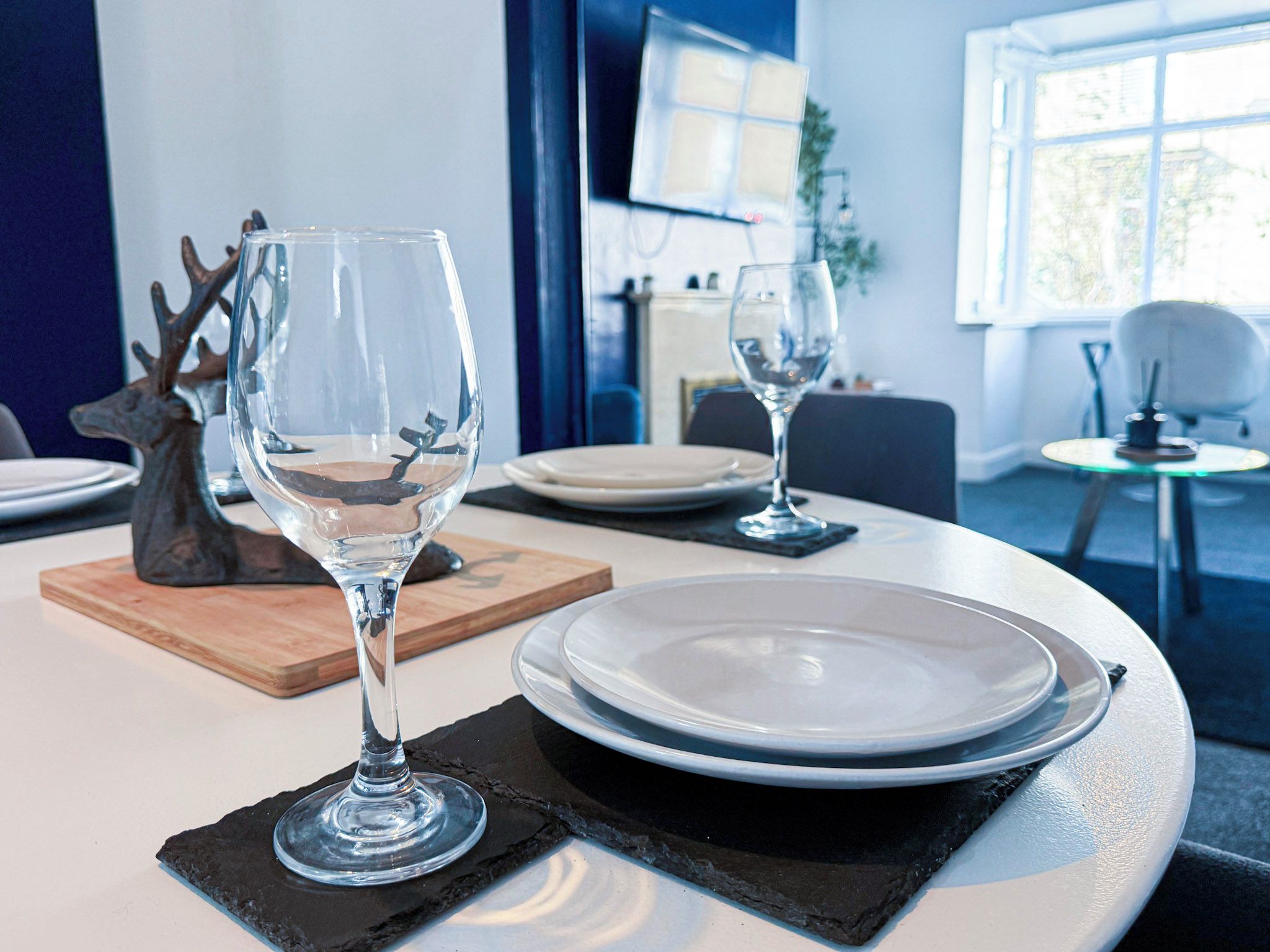 Une table à manger avec deux verres à vin, des assiettes et une figurine de cerf.
