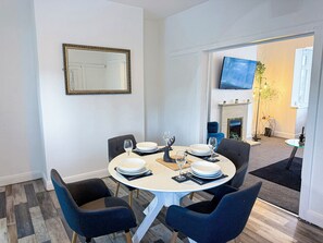 A dining area with a round table set for four, chairs, and a television mounted on the wall.