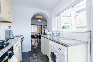 Une petite cuisine équipée d’un lave-linge, d’un évier et d’une fenêtre.