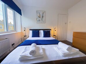 A hotel room with a bed, two bedside lamps, a window, a door, and a painting on the wall.