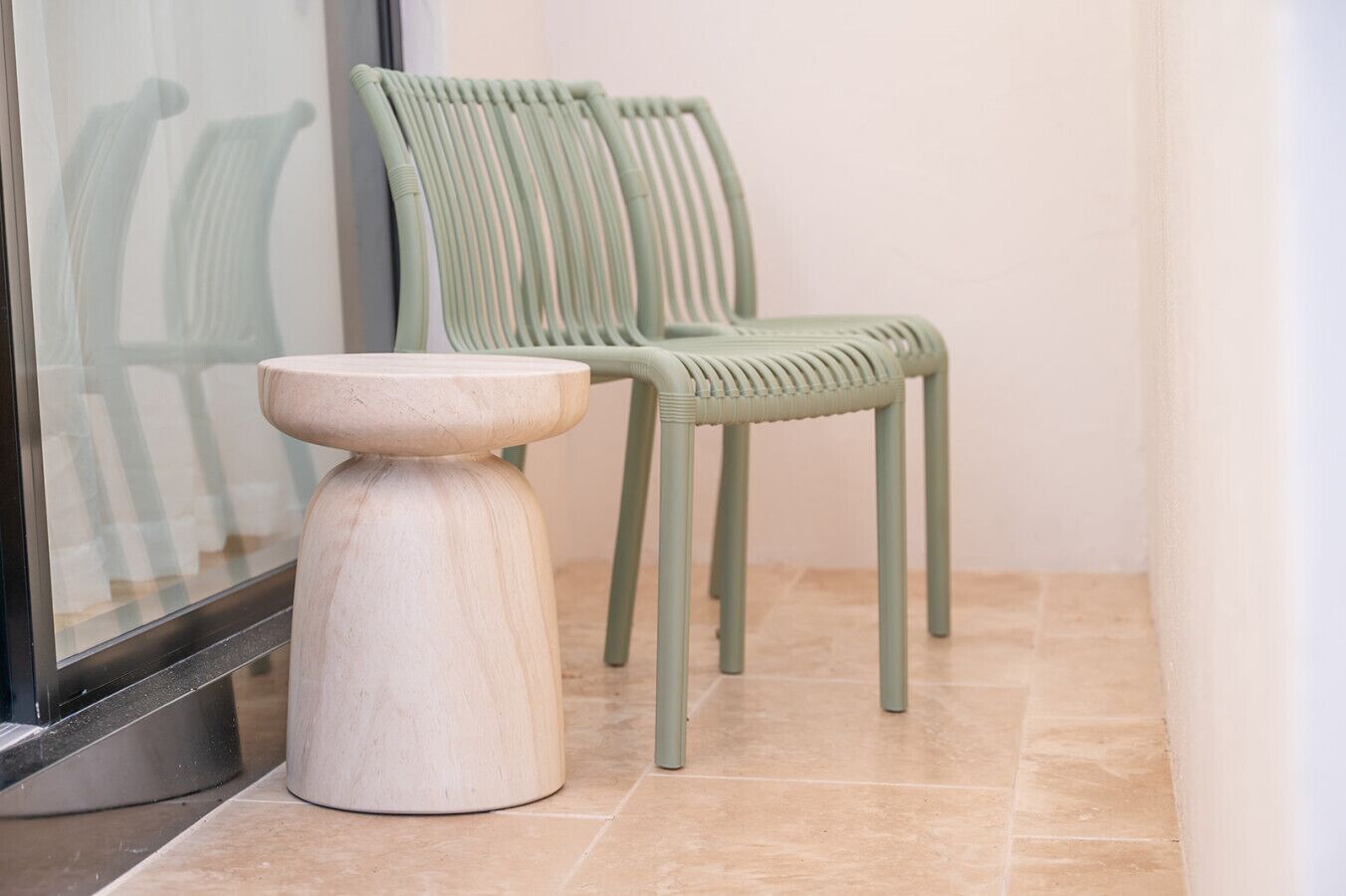 Two green chairs and a wooden stool in a corner with a tiled floor.