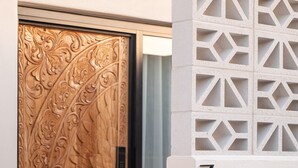 A wooden door with intricate carvings, a glass door next to it, and a white wall with a geometric pattern. - Pacific Sun Bargara ~ by the beach (Bargara)