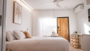 A modern hotel room with a large bed, a ceiling fan, a wooden door, and a small wooden side table. - Pacific Sun Bargara ~ by the beach (Bargara)