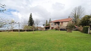 A large, open grassy yard with a two-story house featuring a red-tiled roof and stone walls. - Gîtes de France® - Gîte de Lacroux (LINAC)